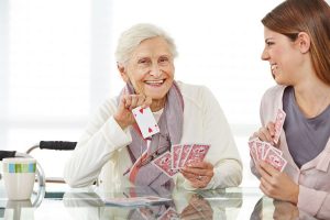 Junge Frau spielt mit einer glücklichen Seniorin im Seniorenheim Karten. Foto: fotolia - Robert Kneschke